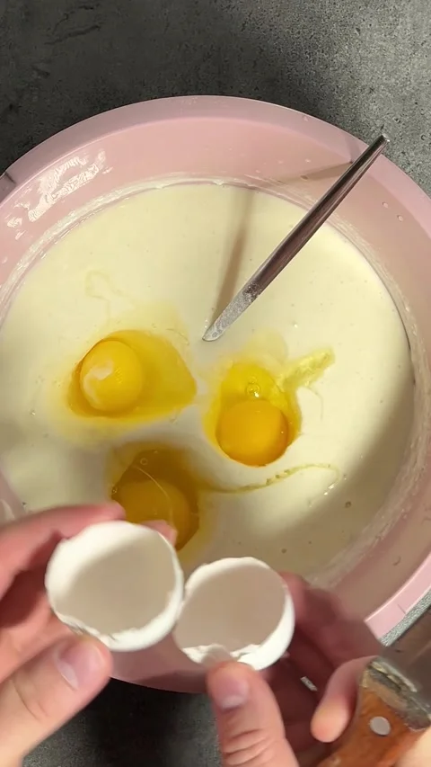 Vertical video close up. Yellow yolk falls into pink bowl with dough Video stock 295573522