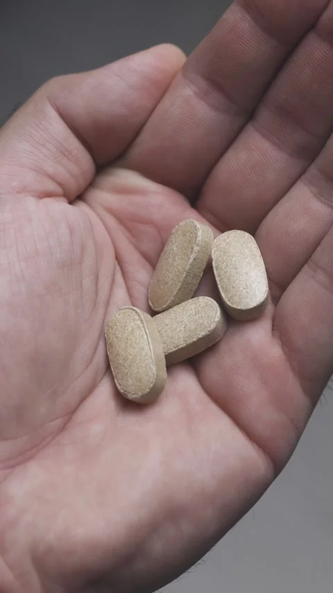 Vertical video closeup of light colored pills poured into open human palm Stock Footage 342240115