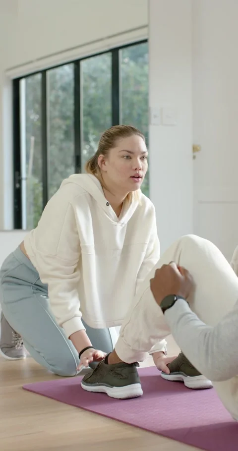 Vertical video: Coach kneeling on purple mat holding shoes as client doing Видео 346735325