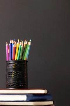 Vertical video of composition of crayons in container on stack of books on grey Foto stock