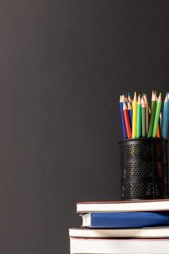 Vertical video of composition of crayons in container on stack of books on grey Stock Photos