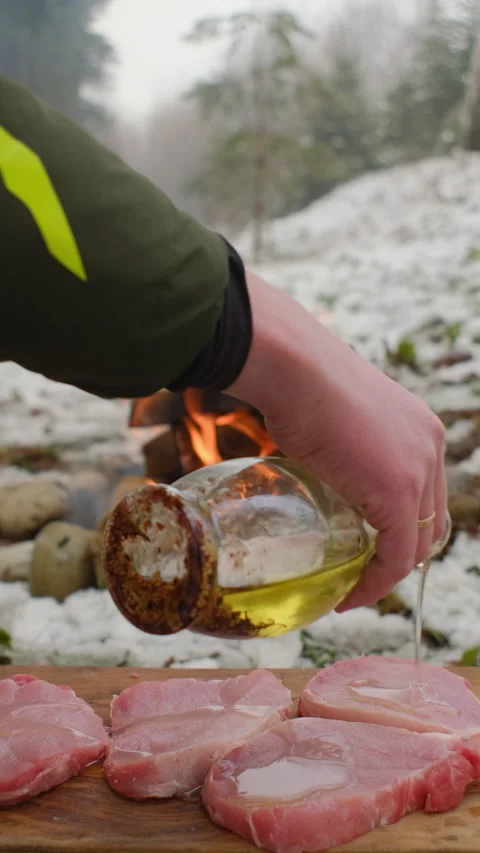 Vertical video of cook generously pours oil over meat before cooking in winter Stock Footage 297944649