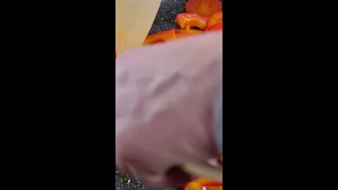 Vertical video. A cook uses two wooden spatulas to stir red paprika in a hot pan Stock Footage 302637425