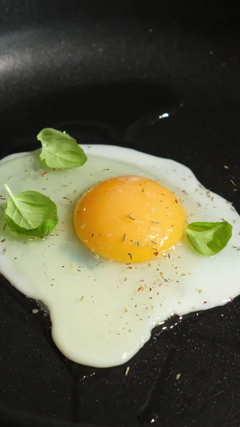 Vertical video. Cooking fried eggs in frying pan. Hands garnish egg with fr.. Stock Footage 340335576