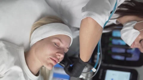 Vertical video. A cosmetologist does hardware facial cleansing for a blonde Stock Footage 295037901