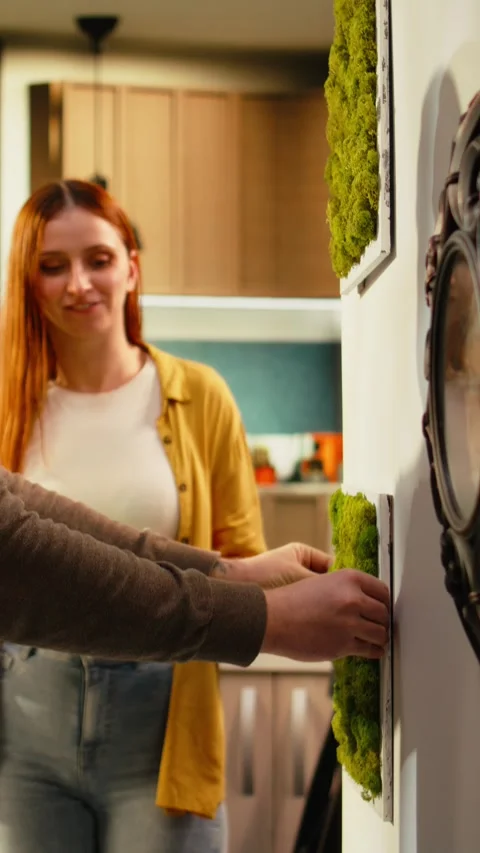 Vertical Video Couple arranging decorations and paintings on the wall in new Stock Footage 343349017