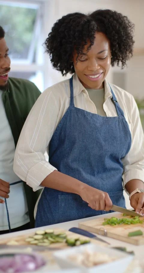 Vertical video: Couple cooking in kitchen, woman chopping on board as man Stock Footage 345093214