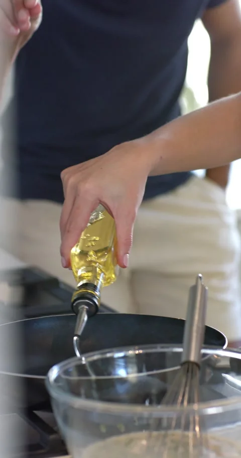Vertical video: Couple cooking in kitchen, female hand pouring oil into pan Stock Footage 345323368