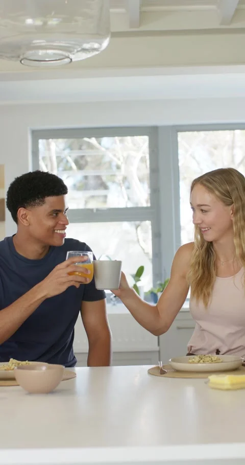 Vertical video: Couple in kitchen having breakfast, woman lifting mug causing Stock Footage 345397583