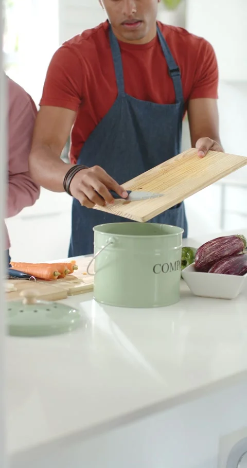 Vertical video: Couple at kitchen island, man scraping board into green bin Stock Footage 345093164