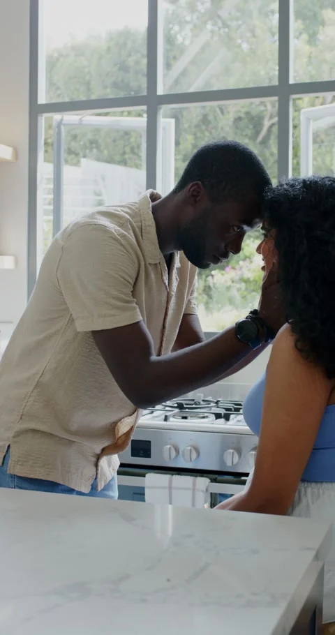 Vertical video: Couple at kitchen island, man reaching, touching woman's cheek, Stockbeeldmateriaal 345218508