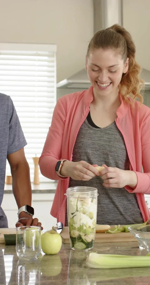 Vertical video: Couple making green smoothie in kitchen after playful bite, Stock Footage 345321135
