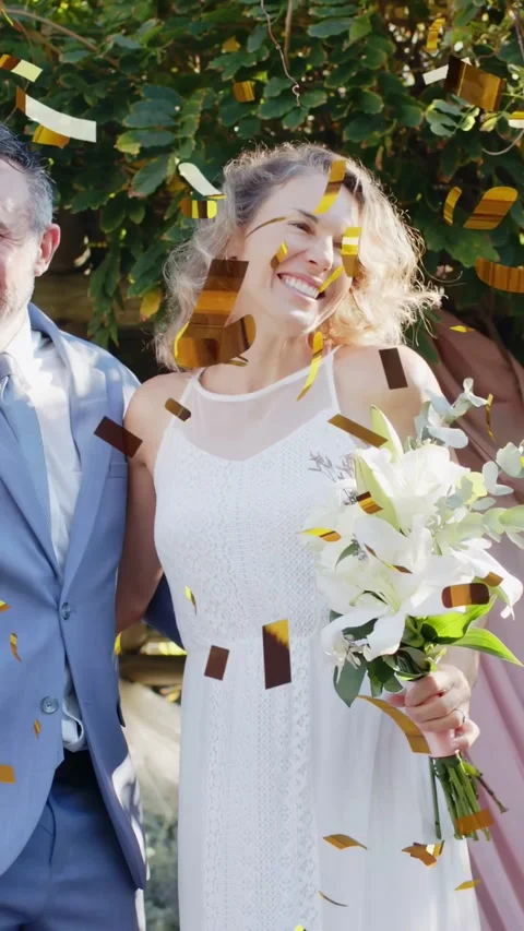 Vertical video: Couple posing in garden, confetti releasing above while holding Vídeo Stock 334770367