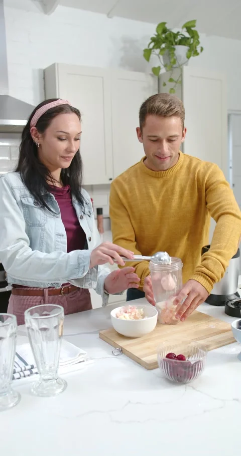Vertical video: Couple prepping smoothie at kitchen island, woman scooping ice Stock Footage 344695160