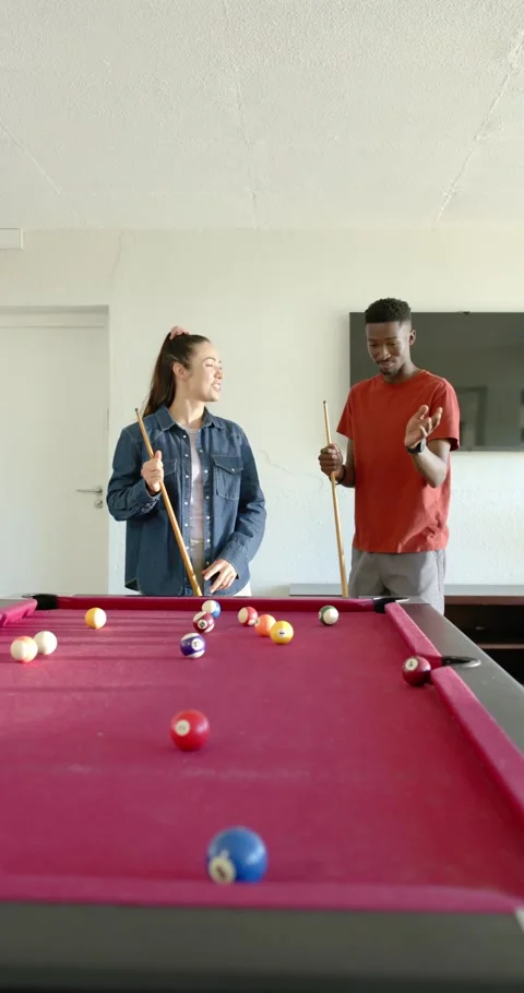Vertical video: Couple standing behind red pool table with cues, noting balls at Stock Footage 337259200