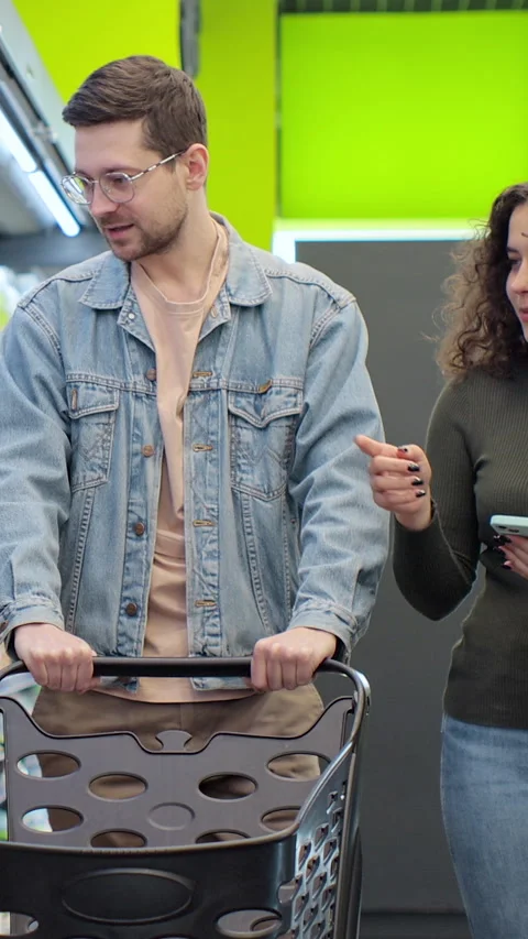 Vertical video. Couple using smartphone in supermarket while grocery shopping. Stock Footage 346683169