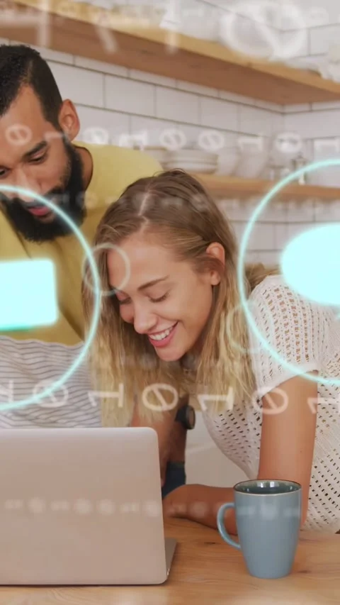 Vertical video: Couple viewing laptop in kitchen, laptop activating tech overlay Stock Footage 333596237
