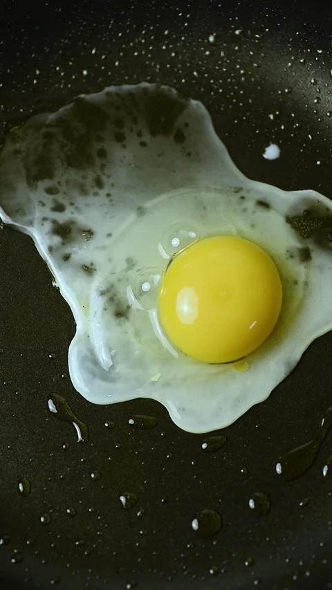 Vertical video of cracking a fresh egg onto a hot frying pan for frying Stock Footage 344893320