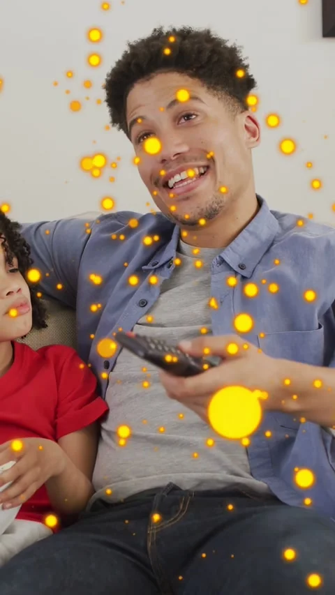 Vertical video: Dad pointing remote at media, amusing child with bowl, orange Stock Footage 333895959