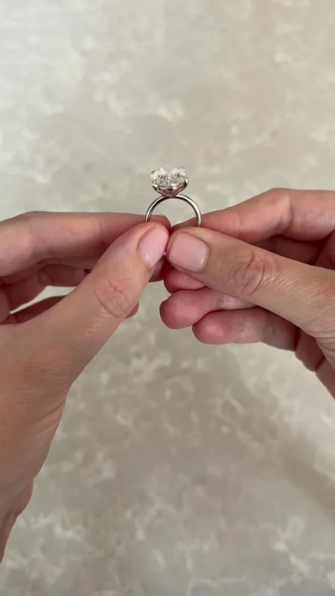 Vertical video delicate hand holding platinum oval diamond engagement ring Stock Footage 316813853