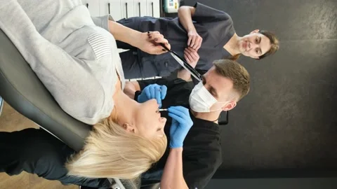 Vertical video, a dentist with an assistant examines teeth with sterile dental Stock Footage 222810806