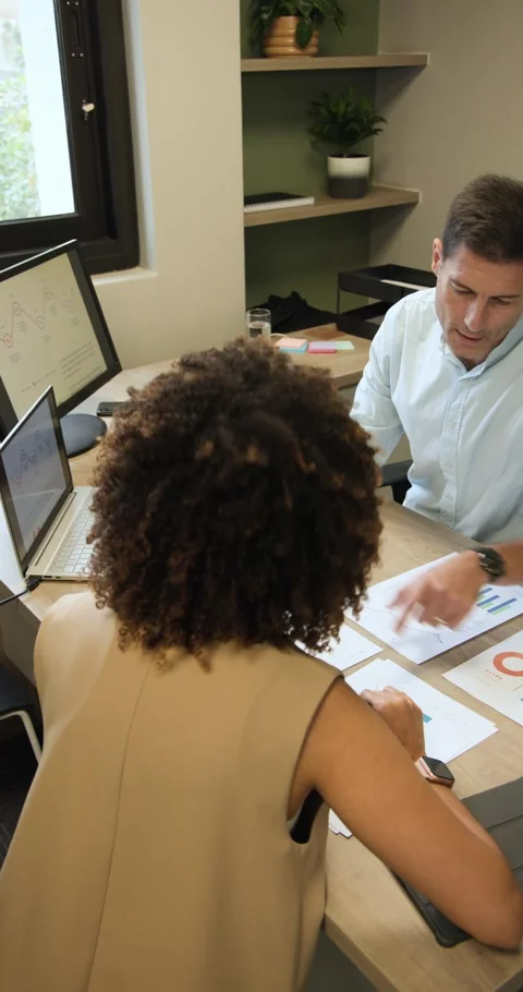 Vertical video: Diverse colleagues sitting at desk pointing at chart and Stock Footage 346718563