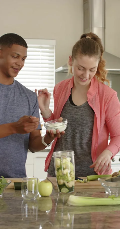 Vertical video: Diverse couple adding yogurt and celery into blender at counter Video stock 345321128