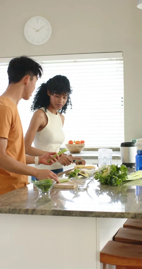 Vertical video: Diverse couple chopping produce at kitchen island, prepping Stock Footage 345217860