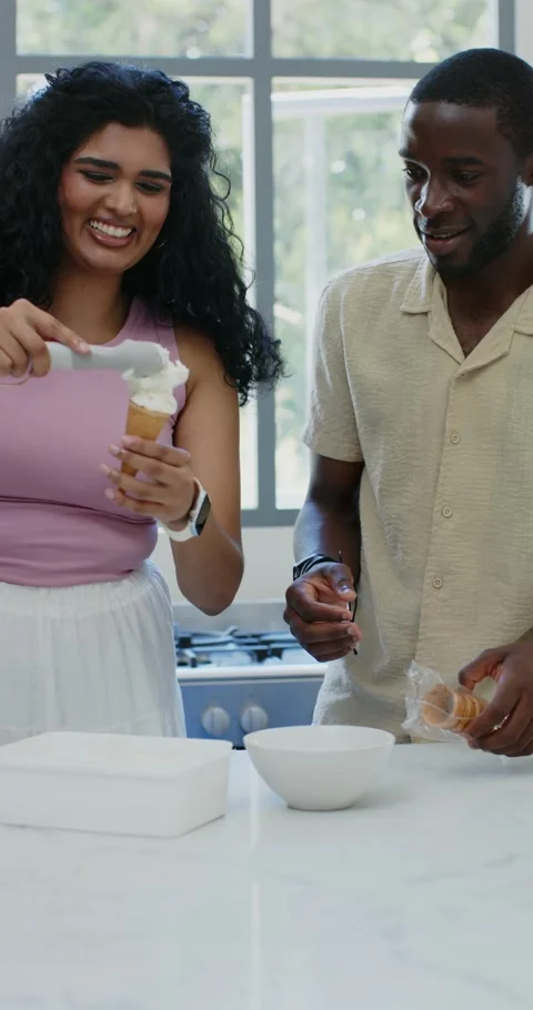 Vertical video: Diverse couple at counter making dessert, woman filling cone Stockbeeldmateriaal 345218543