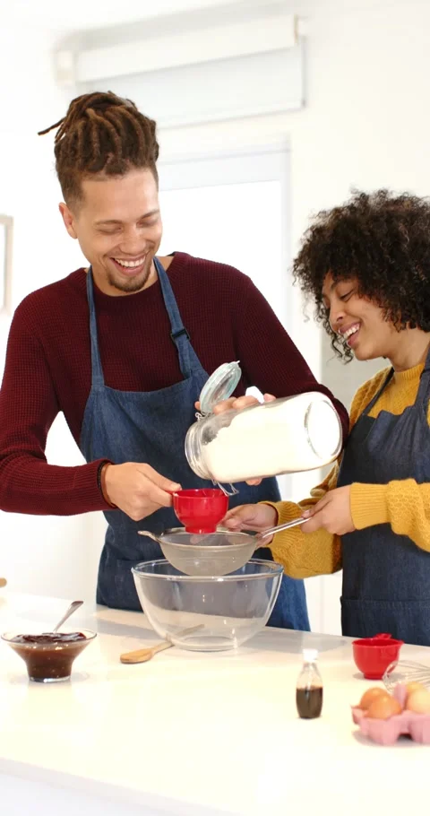 Vertical video: Diverse couple in kitchen removing lid, pouring flour with Video stock 345320712