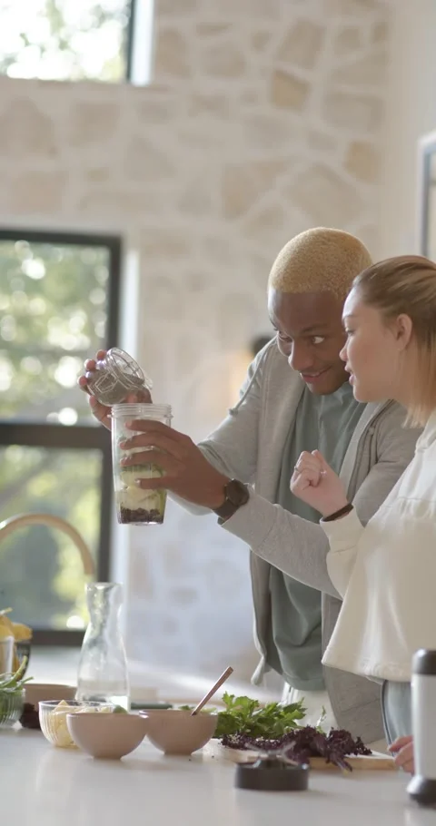 Vertical video: Diverse couple in kitchen lifting glass jar, pouring into Видео 346735337