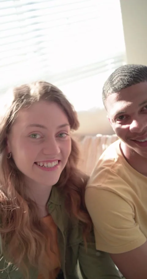 Vertical video: Diverse couple left woman filming phone on couch by blinds, Stock Footage 345395868