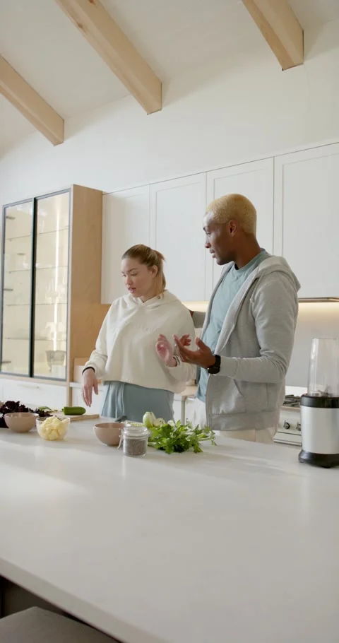 Vertical video: Diverse couple showing phone pointing at items slicing cucumber Видео 346735333