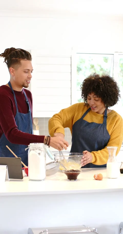 Vertical video: Diverse couple using tablet recipe sprinkling flour and mixing Video stock 345491632