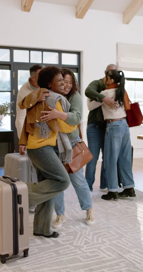 Vertical video: Diverse friends coming in entry area hugging placing luggage Видео 346735365