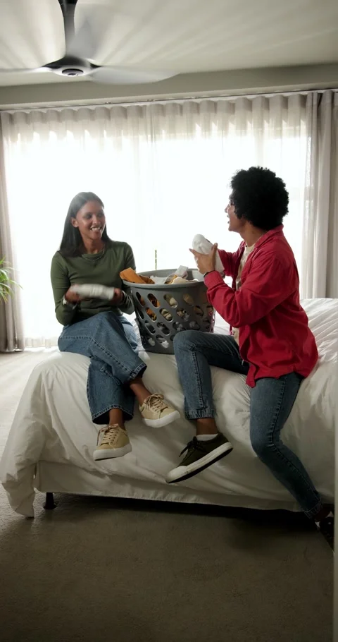 Vertical video: Diverse friends entering room, folding laundry from basket for Vídeo Stock 345319961