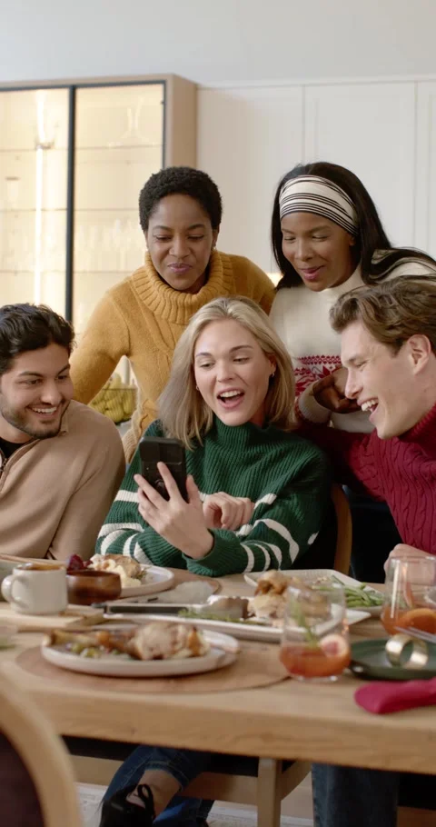 Vertical video: Diverse friends leaning at table, woman scrolling phone causing Видео 346735318