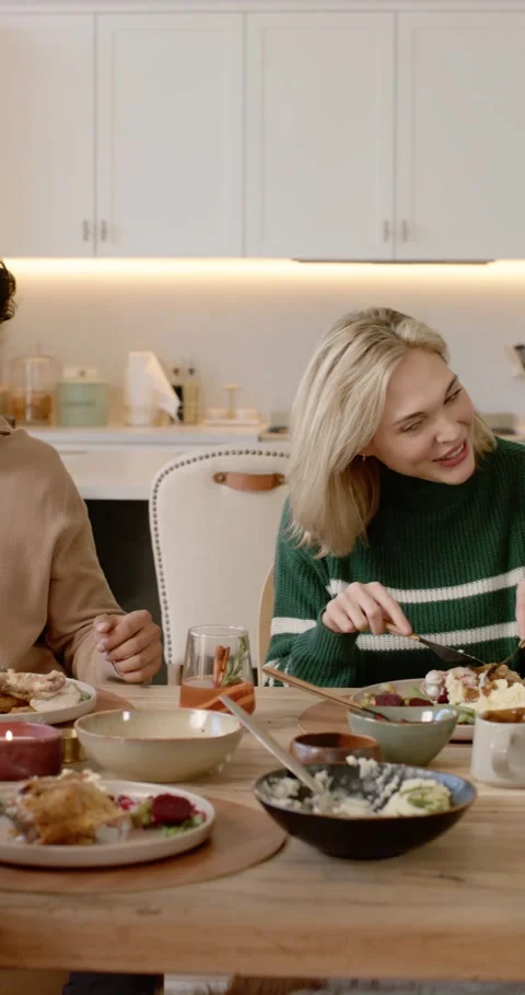 Vertical video: Diverse friends passing bowls at kitchen table, cutting food and Видео 346735317