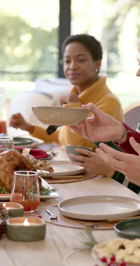 Vertical video: Diverse friends in sweaters passing bowl at table reaching Видео 346735291