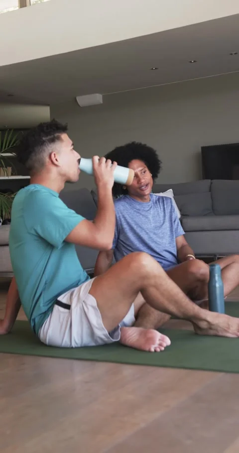 Vertical video: Diverse men on mat at home, exercise thirst driving bottle Stock Footage 346721706