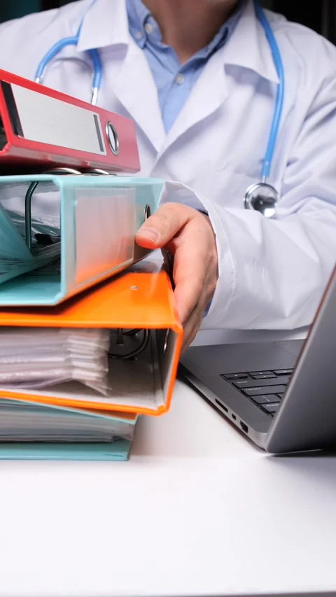 Vertical video doctor sorting through a stack of patient files and binders Stock Footage 324766734