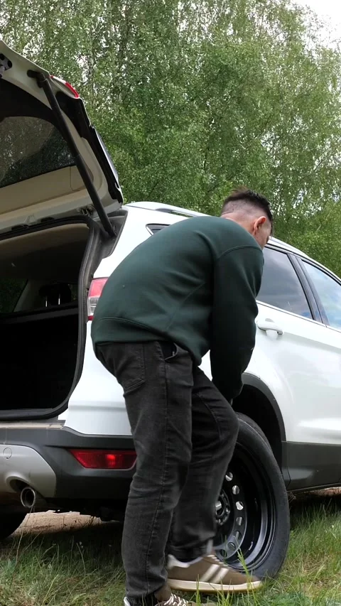 Vertical video driver takes out spare tire from the trunk of car. flat tire Stock Footage 276238542
