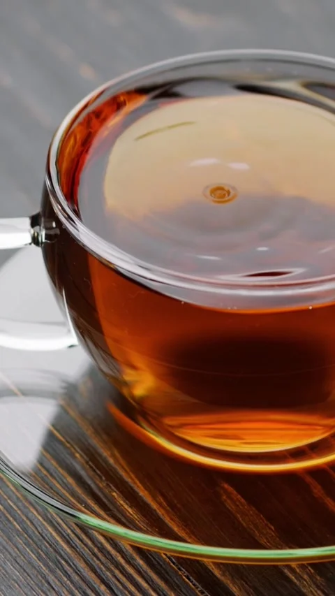 VERTICAL VIDEO: Drops of fragrant black tea fall into transparent cup with tea Stock Footage 270944285