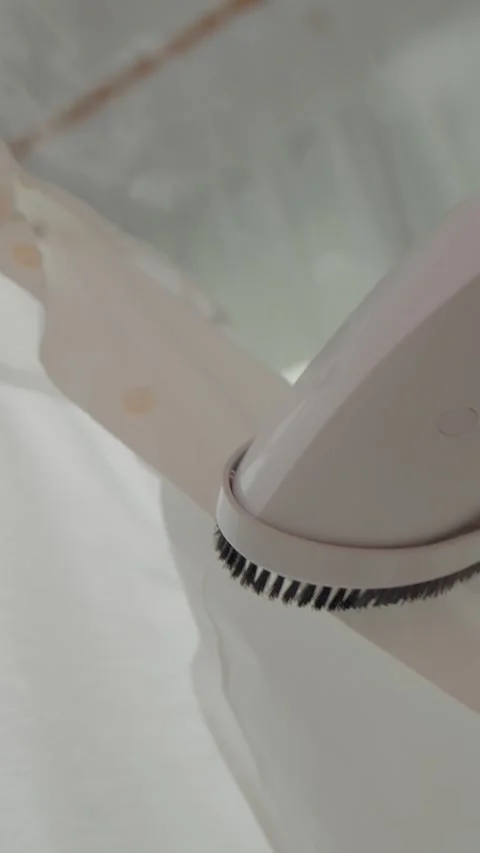 Vertical video Efficiently smoothing clothes with a handheld steamer in a home Stock Footage 327598660