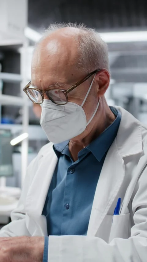 Vertical video Elderly scientist wearing surgical mask working on laptop in lab Stock Footage 325681033