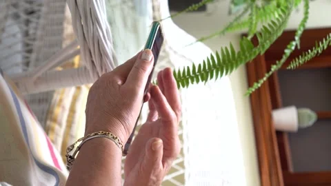 Vertical video: elderly woman using a mobile phone in a bright courtyard at h Stock Footage 164392594