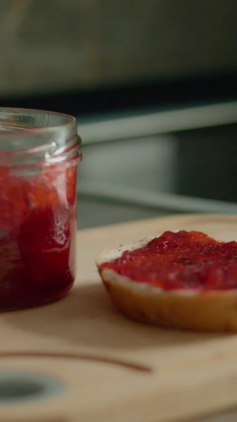 Vertical video Enjoying a slice of bread topped with raspberry jam on a kitchen 스톡 동영상 323363921
