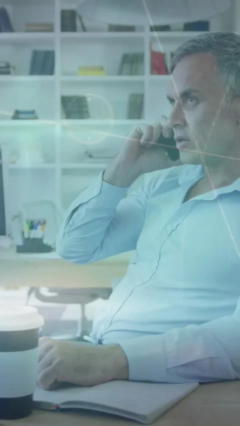Vertical video: Exec taking call, noting and reaching cup for project, overlays Stock Footage 331047308