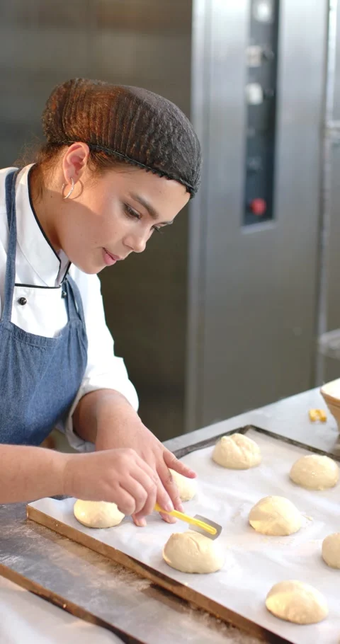 Vertical video: Female baker checking dough, scoring rolls with yellow scraper Stock-Footage 346724190