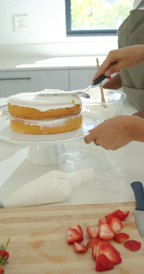 Vertical video: Female baker in green apron dipping spatula, smoothing cake Stock-Footage 346724433